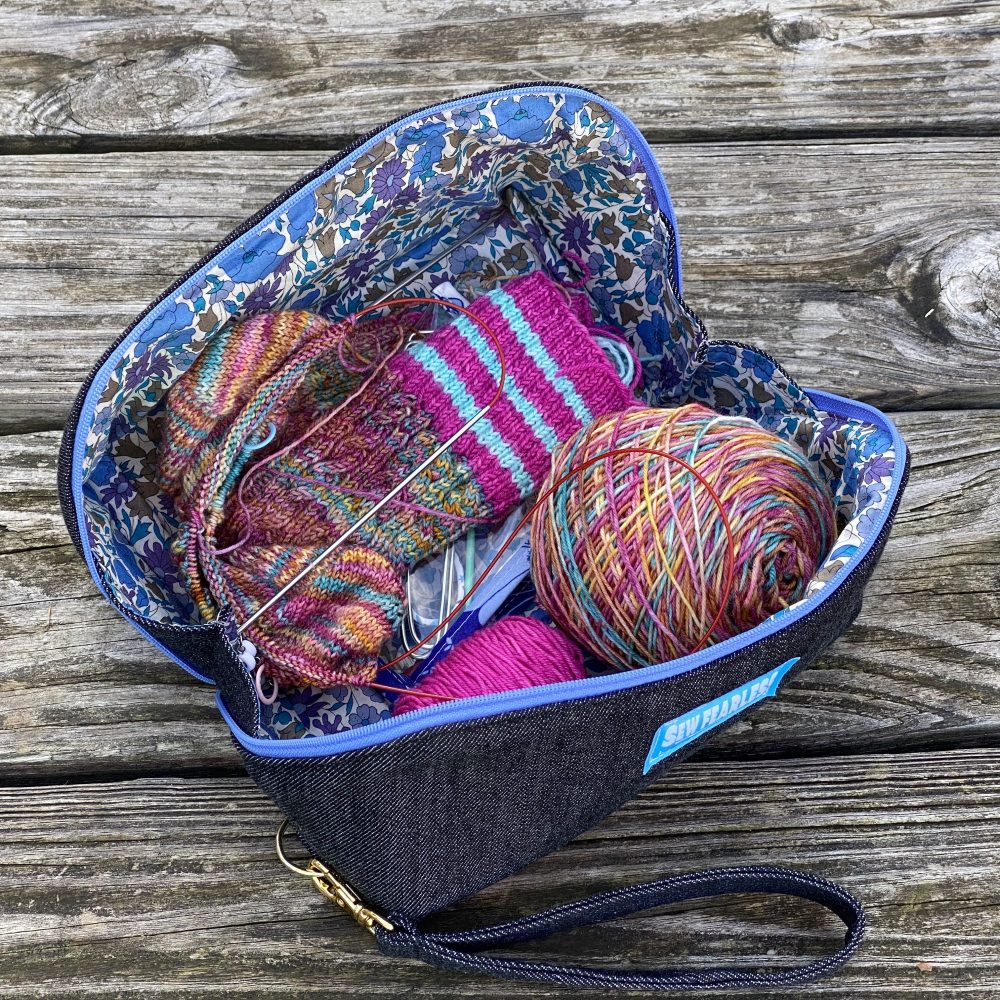 open denim pouch with bright pink and blue sock knitting project, on wood background